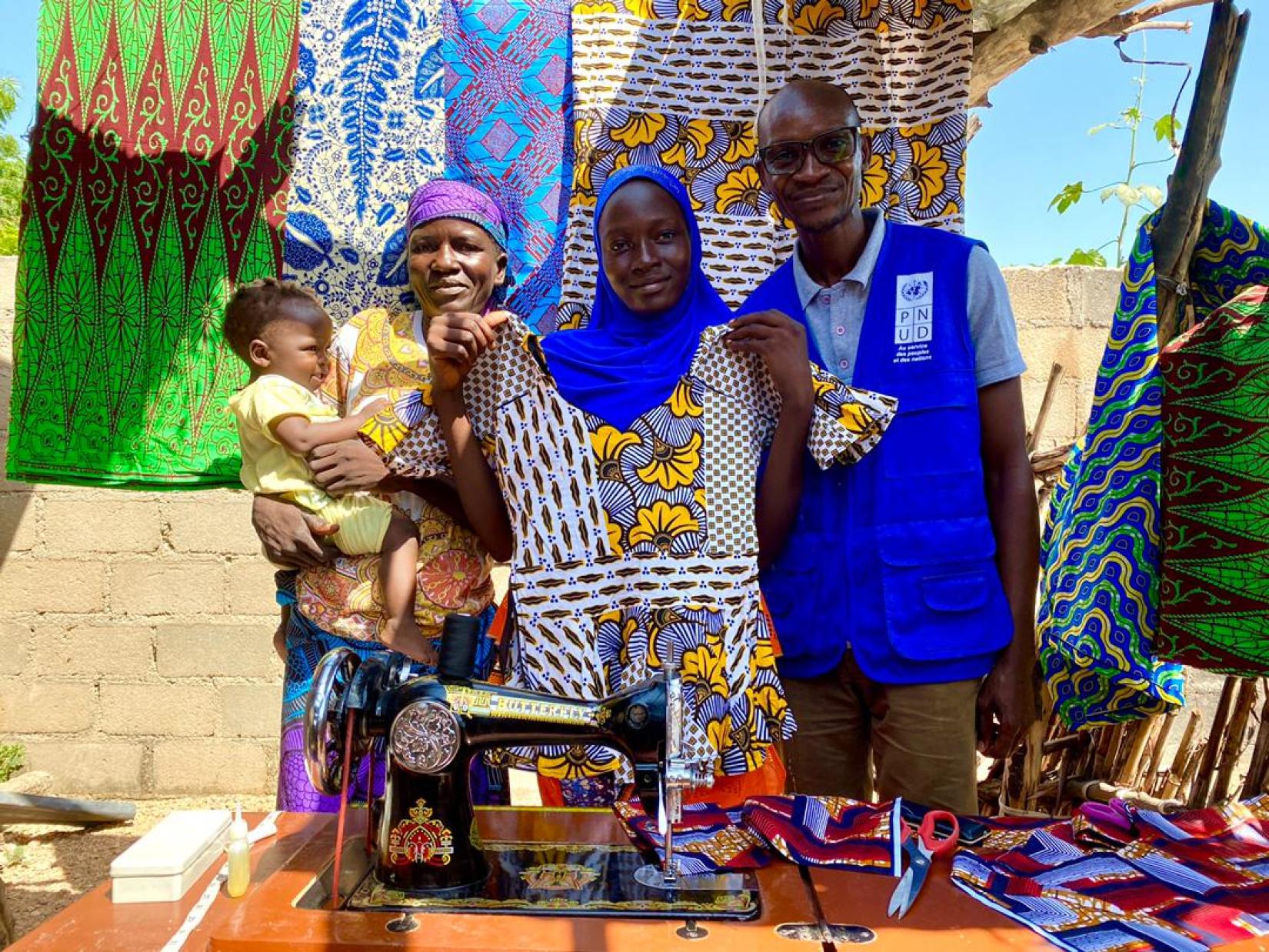 Marguerite happily showcases one of her designs; her mother and youngest sister can now smile for a bright future